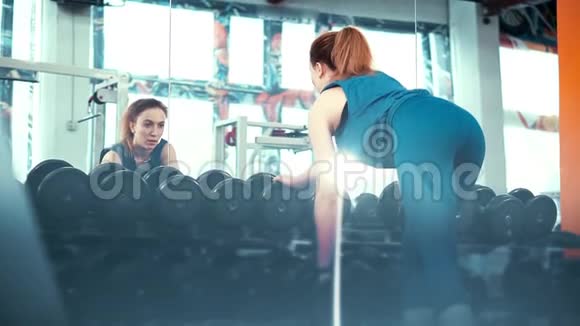 宽框年轻的健身女孩在一面巨大的镜子前用哑铃做运动视频的预览图