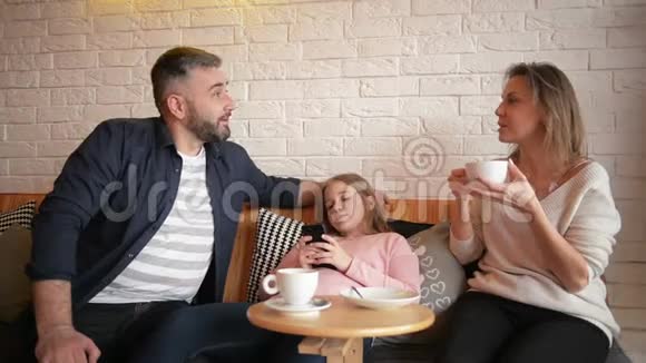 家庭在咖啡厅休息家庭是母亲父亲和女儿人们坐在桌子旁他们快乐微笑视频的预览图