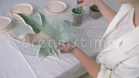 手工制作的陶器熟练的女艺术家在车间用刷子在陶器上作画视频的预览图