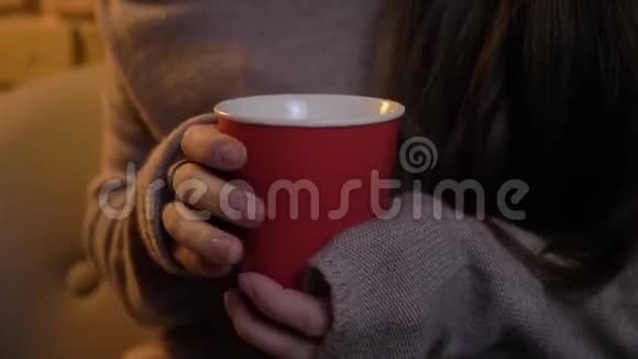 在舒适的家庭背景下年轻的白种人女孩用红色杯子享受热饮的特写肖像视频的预览图