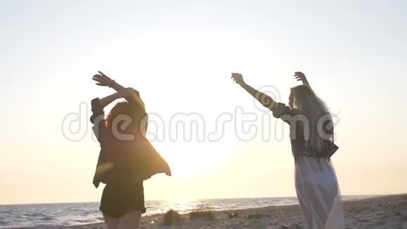 两个年轻性感的女人在海边夕阳的余晖中穿着波霍风格的沙滩上跳舞视频的预览图