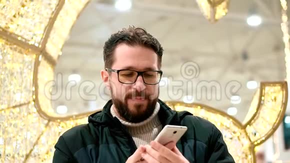 戴眼镜的胡子男看着智能手机在电话里说话视频的预览图