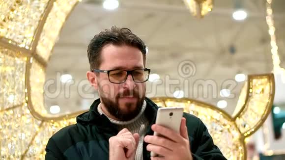 戴眼镜的胡子男看着智能手机发出语音信息视频的预览图