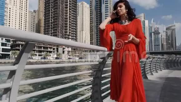 一个穿着鲜红色裙子的混血女孩沿着迪拜码头走着在电话中赞赏地交谈着阿拉伯联合组织视频的预览图