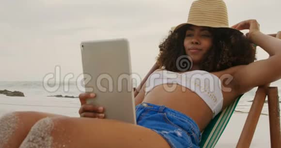 非洲裔美国妇女在海滩上使用数字平板电脑的正面景色视频的预览图