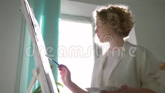 有灵感的画家妇女与缪斯绘画与明亮的颜色在白色画布上的画架艺术课在阳光下视频的预览图