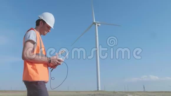 一个人在风力涡轮机的背景下控制着一个无人驾驶飞机用复印机检查风力涡轮机这就是视频的预览图