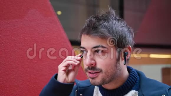 英俊的年轻人戴着无线耳机站在城市背景下视频的预览图