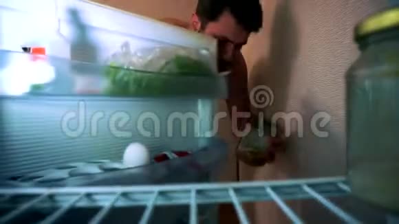 一个穿短裤的人打开冰箱他半空露出脸把罐子放进冰箱里视频的预览图