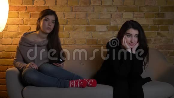 年轻的白种人女孩坐在沙发上在舒适的家庭背景下专心看电视的特写肖像视频的预览图