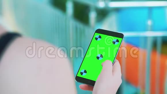 一个年轻女孩用绿色屏幕握着智能手机的手的特写视频的预览图