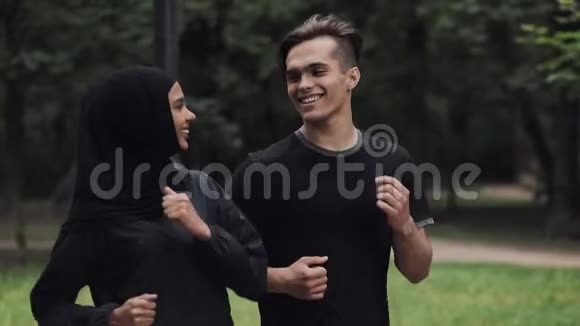 年轻的高加索人和穿着Hijab的穆斯林女人看起来兴奋和放松微笑和聊天在公园里奔跑视频的预览图