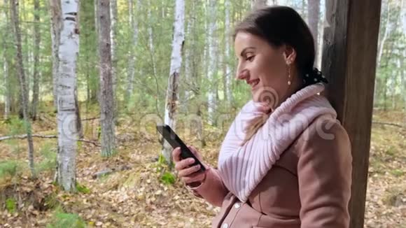 在秋天的春天森林里快乐迷人的女人通过电话在社交网络上交流视频的预览图