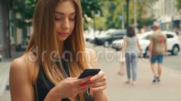 美女在手机上打字背景是街上行人棕色头发的女人看着视频的预览图
