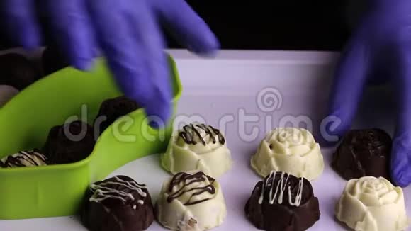 一个戴着橡胶手套的人把巧克力从托盘里放进容器里白色和黑色巧克力中的釉糖国际视频的预览图