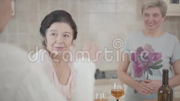 三个成熟的女人在厨房里和桌上的酒聊天一位女士一边打手势视频的预览图