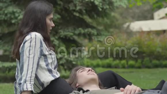 年轻的一对穿着休闲服装的夫妇在户外聚会约会坐在草地上的女孩她视频的预览图