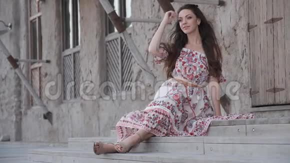 穿着连衣裙的微笑女孩在旧房子的石阶上摆姿势视频的预览图