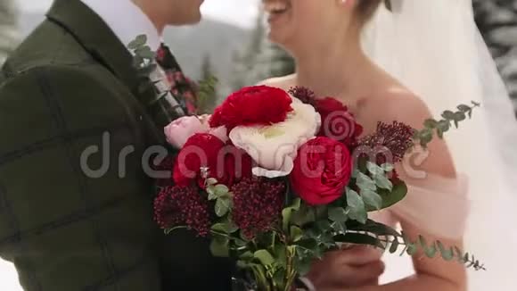 新娘捧着一束由白色和红色玫瑰制成的花新婚夫妇在雪地里拥抱亲吻和抚摸视频的预览图