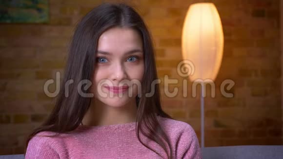 一个年轻可爱的黑发白种人女孩坐在沙发上看着摄像机高兴地笑着特写镜头视频的预览图