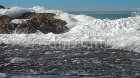 在海岸线附近的棕色岩石上翻滚着泡沫的海浪视频的预览图