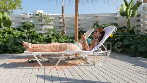 穿比基尼的女士在家晒日光浴的时候可以用智能手机放松视频的预览图
