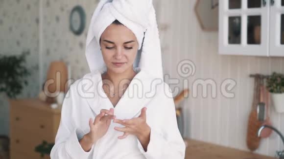 闭上眼睛头上有毛巾的女孩在脸上涂抹保湿霜动作缓慢视频的预览图