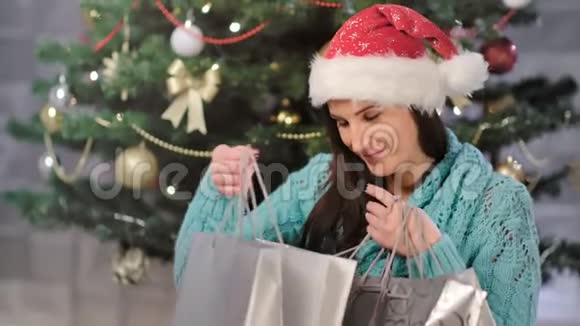 期待节日的欧洲妇女微笑并在装饰圣诞树附近打开礼品包视频的预览图
