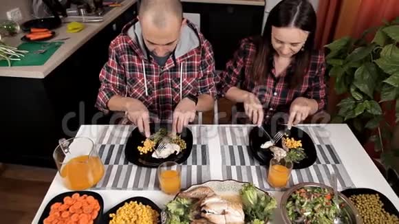 夫妻俩坐在餐桌旁的厨房里吃晚饭桌子上有沙拉蔬菜蔬菜鸡肉玉米视频的预览图