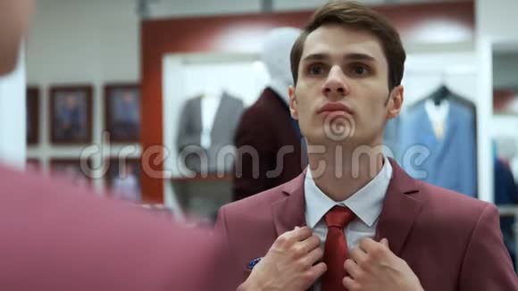 男人看着镜子穿着一件红夹克在精品店里视频的预览图