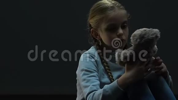 小女孩抱着玩具熊坐在黑暗的空房间里缺乏父母的照顾视频的预览图