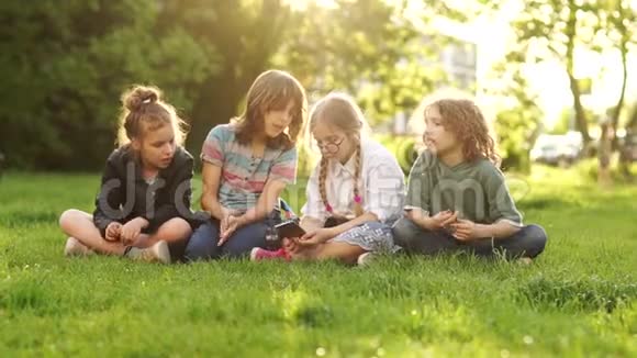 一群青少年在课间休息时坐在草地上四个男孩和女孩观看并讨论视频的预览图