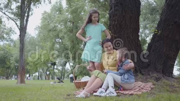成熟快乐的祖母一边教她的孙女一边坐在绿色大树附近美丽的公园里妇女视频的预览图