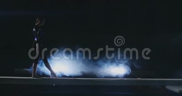 职业体操运动员女孩在平衡木上缓慢地旋转一跳烟色蓝色视频的预览图
