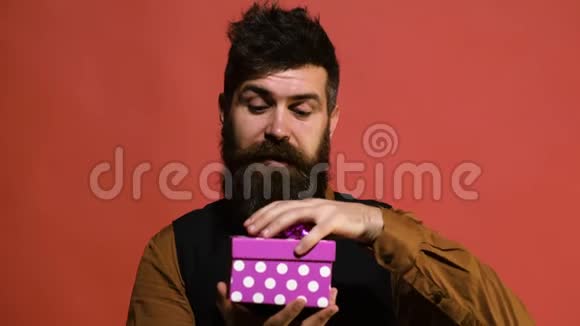 大胡子男子打开礼品盒时惊喜万分男人打开一个粉红色的盒子红色背景上有一个礼物节日视频的预览图