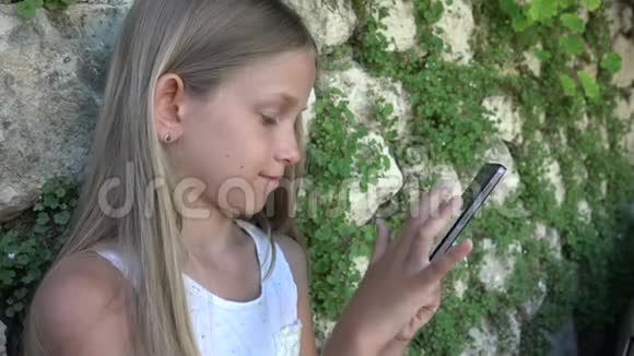 庭院石墙儿童玩智能手机女孩使用平板电脑儿童户外视频的预览图