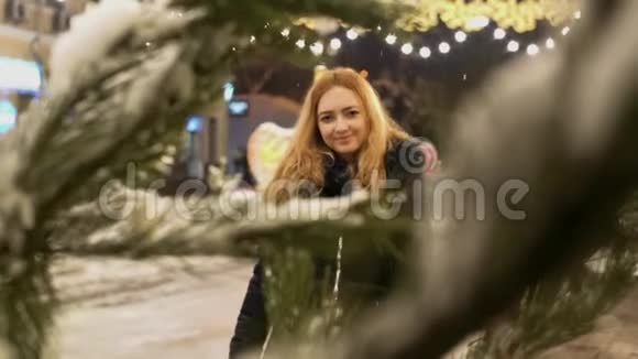 年轻微笑的女人走近镜头前景中的圣诞树树枝视频的预览图