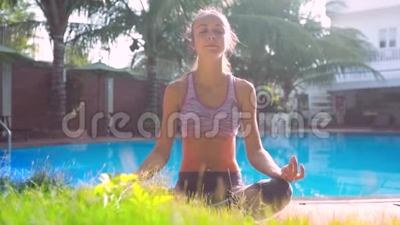 美丽的女孩坐在瑜伽姿势莲花对泳池棕榈酒店视频的预览图