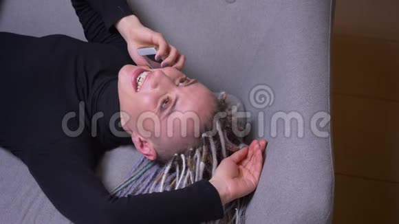 一位年轻迷人的白种人女性金发美女躺在沙发上打电话的特写镜头视频的预览图