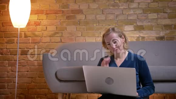 白种人的一位年长女性坐在室内的地板上看着笔记本电脑上的节目视频的预览图