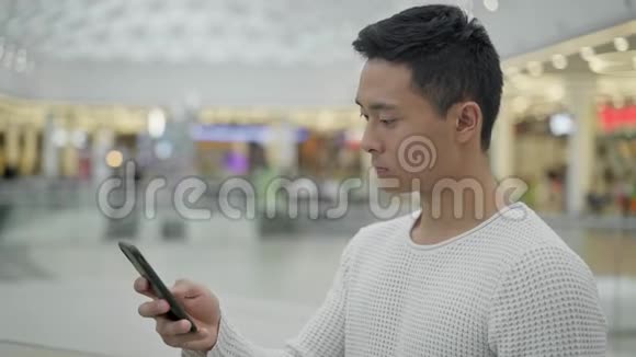 大商场背景下亚洲男性滚动手机中档视频的预览图