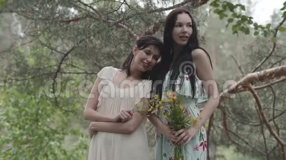两个穿着短裙的漂亮女孩站在岩石上开着野花看着森林视频的预览图