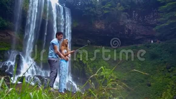 拥抱情侣用热带瀑布和岩石自拍视频的预览图