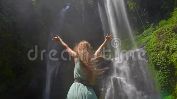 年轻女性游客参观巴厘岛最大的瀑布塞库普尔瀑布慢镜头旅费视频的预览图