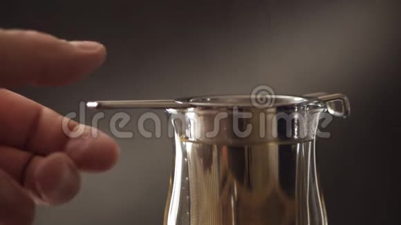 用金属过滤器在玻璃杯中酿造茶特写一个男人手蘸着一个带茶叶的钢制过滤器视频的预览图