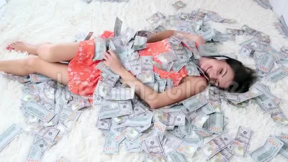 美丽的女孩享有巨大的财富女人躺在一张白色的床上身上有很多钱一堆美元钞票视频的预览图