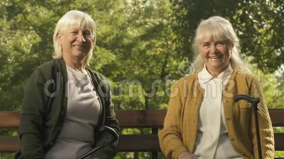 快乐的老年妇女举起手杖坐在长凳上胜利者的姿态视频的预览图