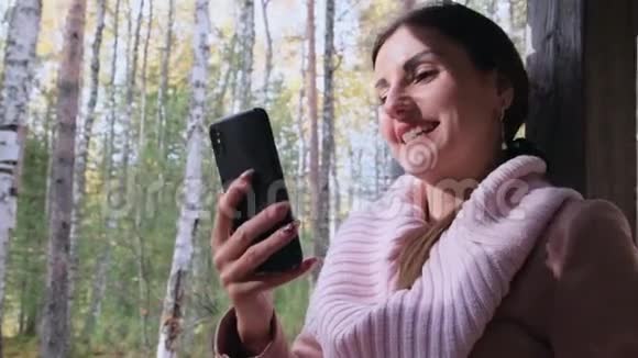 在秋天的春天森林里快乐迷人的女人通过电话在社交网络上交流视频的预览图