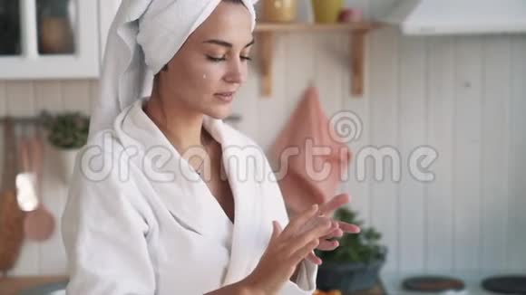 靠近点头上有毛巾的女人在脸上涂抹保湿霜动作缓慢视频的预览图
