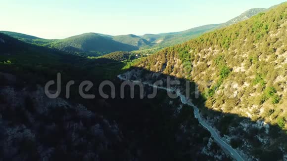 在阳光明媚的夏日高山之间的道路被绿树和灌木覆盖在蓝天上视频的预览图